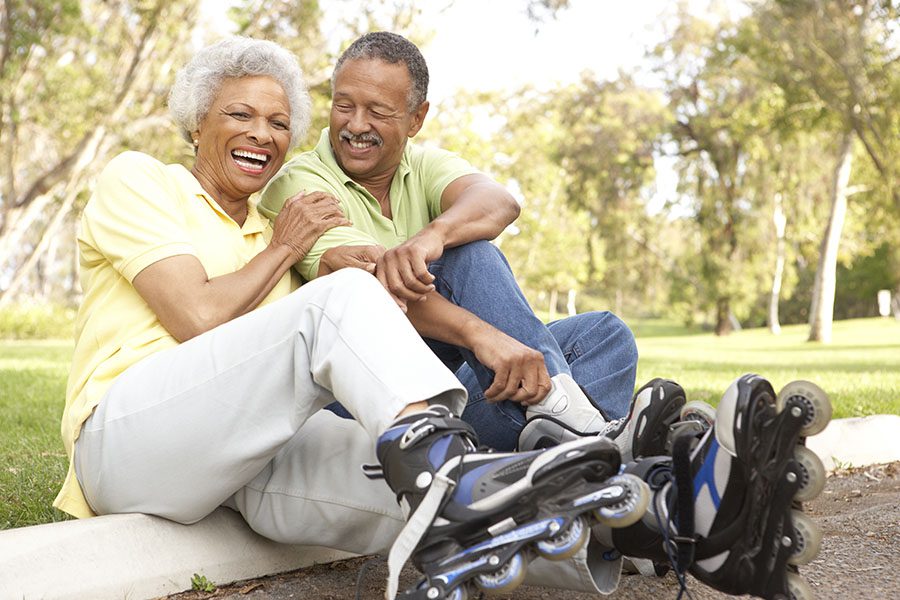 Other Insurance - Laughing Elderly Couple At The Park Putting On Rollerblades