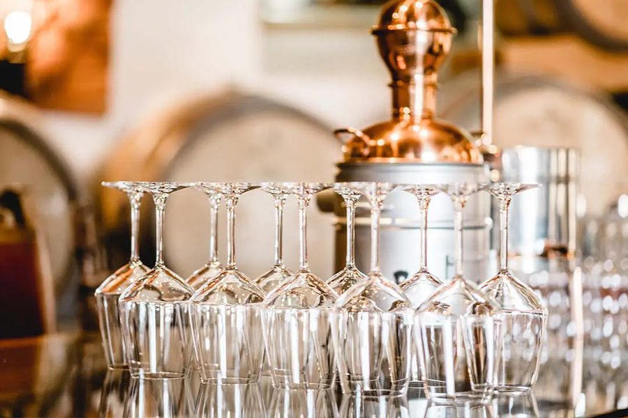 Distillery Insurance - Close up of an Glassware and an Alembic Still Used for Making Alcohol inside a Distillery with Whisky Barrels in the Background